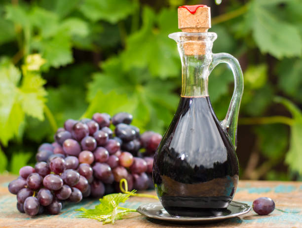 czarny stary ocet balsamiczny w szklanym dzbanku ze świeżymi czerwonymi winogronami na zielonym tle winnicy - balsamic vinegar vinegar bottle container zdjęcia i obrazy z banku zdjęć