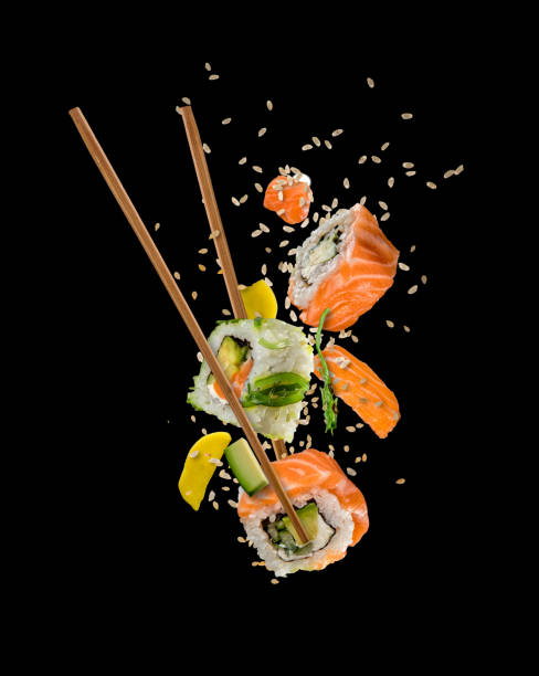 Sushi pieces placed between chopsticks on black background Sushi pieces placed between chopsticks, separated on black background. Popular sushi food. chopsticks photos stock pictures, royalty-free photos & images