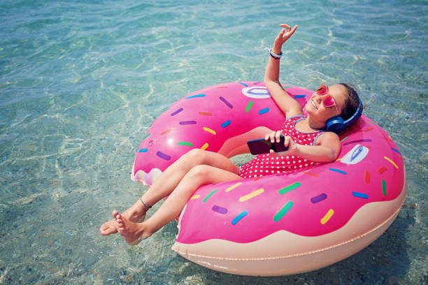 маленькая девочка слушает музыку и танцует в плавающей пончик - sea swimming greece women стоковые фото и изображения