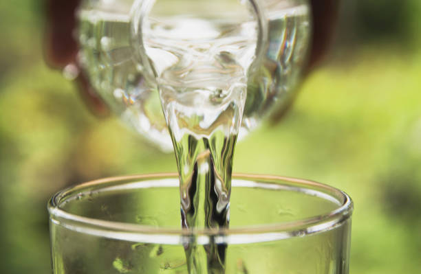istock Person pouring water from bottle to glass on nature background 806387446