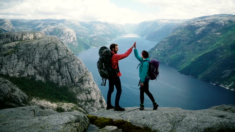 Young Caucasian couple hiking near Preikstolen and giving high five at Lysefjorden