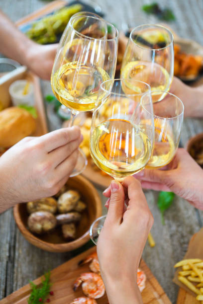 People with white wine toasting over served table with food. Hands with white wine toasting over served table with food. Friendship and happiness concept fusion food photos stock pictures, royalty-free photos & images