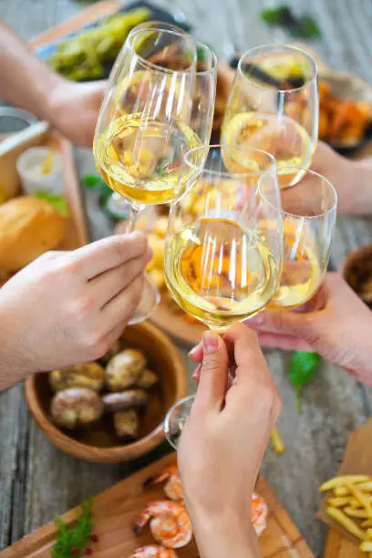 Hands with white wine toasting over served table with food. Friendship and happiness concept