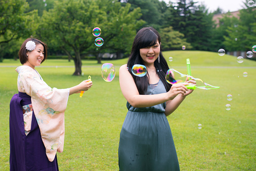 Happy graduates playing with bubbles in green field