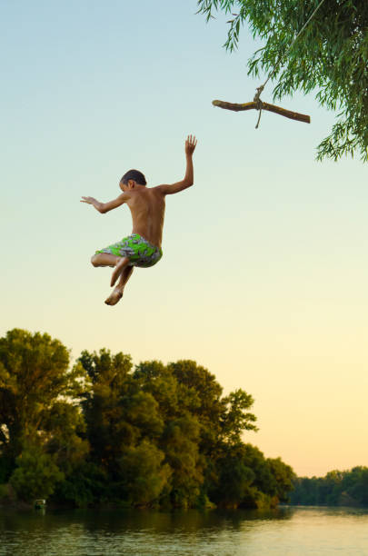 istock Boy jumping into the river from the swinging rope 806511648