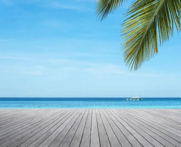 Photo of Wooden platform under palm trees beside tropical sea