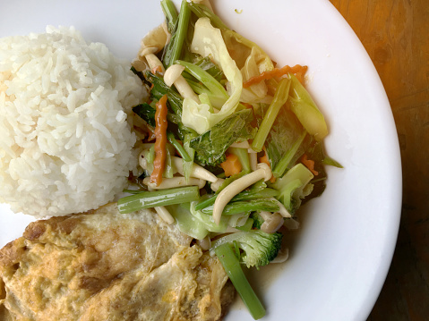 stir fried vegetables with Thai Omelette (scrambled eggs) with rice in white plate on rustic wooden background. Vegetarian Food, healthy food.