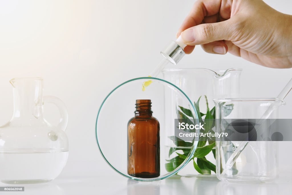 Recipientes de cosméticos garrafa marrom e vidraria científica, foco em óleo caindo em pacote de rótulo em branco para a marca mock-up - Foto de stock de Laboratório royalty-free