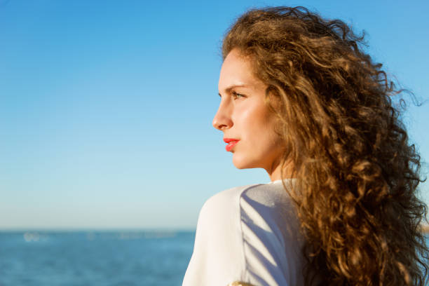 istock Young lady with long curly hair looking far  on the beach 806624252