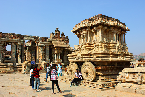 A group of young girls clicking photographs in front of the famous Stone Chariot at Vittala temple in Hampi, Karnataka state, India. Experts say the chariot is actually a shrine housing an icon of Garuda, the vehicle of Hindu god Vishnuand wheels of the chariot are said to be have been inspired by the Sun Temple at Konark, India. The Vittala temple at Hampi is one of the largest temples built in the period 1422-46 A.D by Vijayanagar empire. Hampi is a UNESCO heritage site and is famous for ancient ruins of temples.