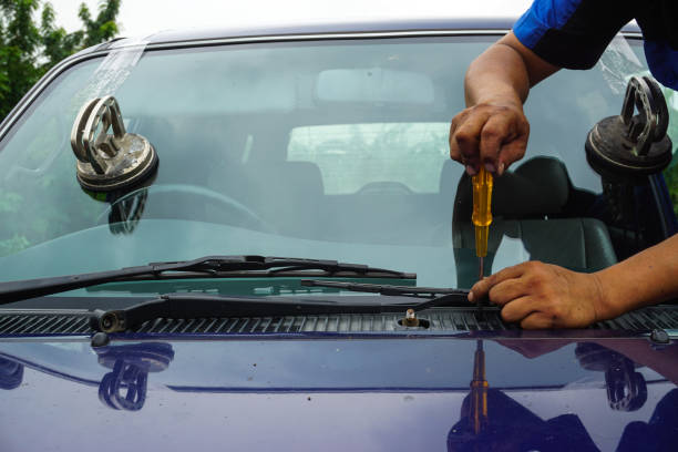 Glazier using tools repairing to fix crack broken windshield on the front window glass.