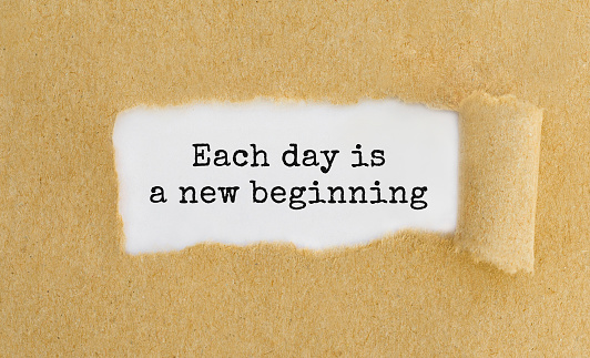 Text Each day is a new beginning appearing behind ripped brown paper