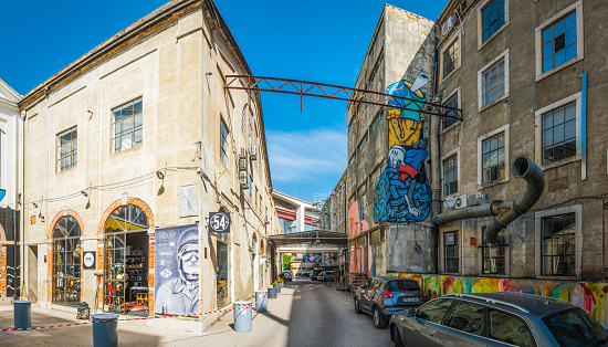The hipster cafes, design studios and fashionable shops of the LX Factory creative quarter under the iconic span of the 25 de Abril Bridge in the heart of Lisbon, Portugal’s vibrant capital city.