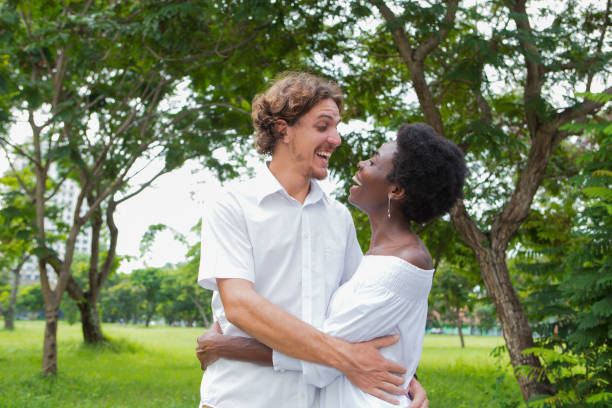 fröhliches paar umarmen und lachen im park - wedding african descent american culture bride stock-fotos und bilder