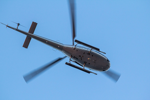 Small, private Helicopter while flying on blue clear sky, bottom view