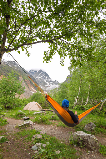 Woman traveler relaxing in hammock in the mountains, next to glacier and admiring beautiful view. Camp with magic view. Wide angle of shooting.