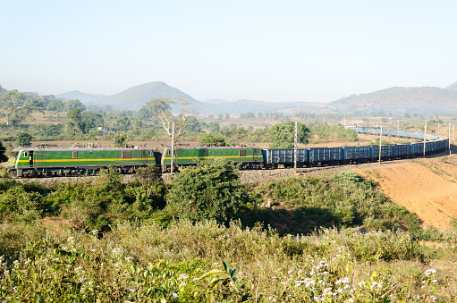 A freight train in  rural India with two locomotives hauling the wagons.