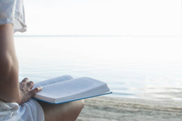 istock Woman reading book at beach, close up. 806796550
