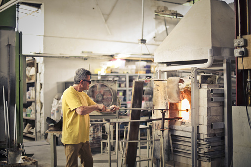 Middle-aged man working in a glass factory heating glass in a furnace