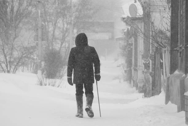 istock Lonely elderly man with a cane walking leisurely through a snow storm through the streets of the city 806822462