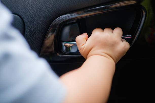 Little Asian 18 months / 1 year old baby boy child holding on to the door handle inside of the car stock photo