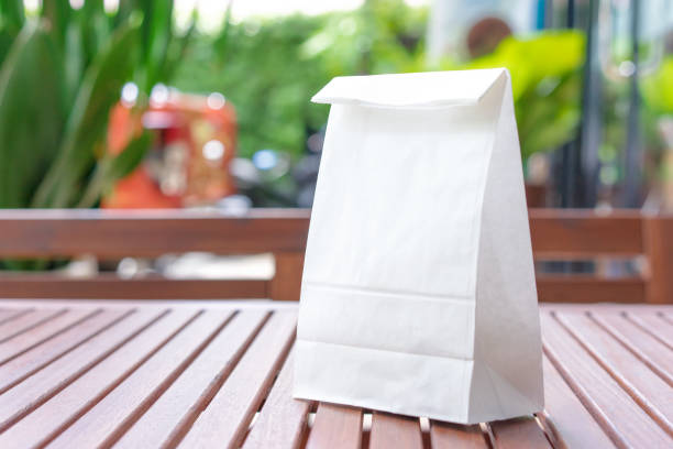 Blank white paper bag for taking out food on a wooden table Blank white paper bag for taking out food on a wooden table packed lunch photos stock pictures, royalty-free photos & images