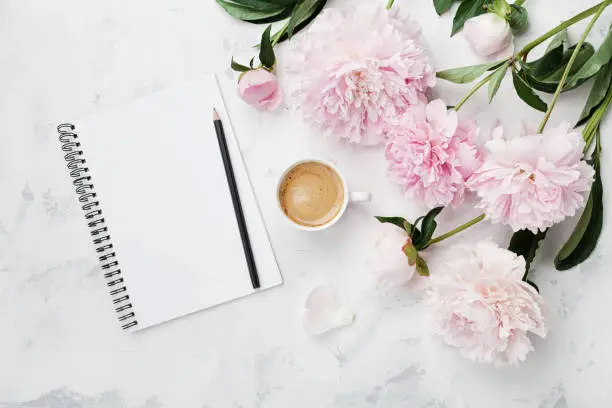 Photo of Morning coffee mug for breakfast, empty notebook, pencil and pink peony flowers. Flat lay. Woman working desk.