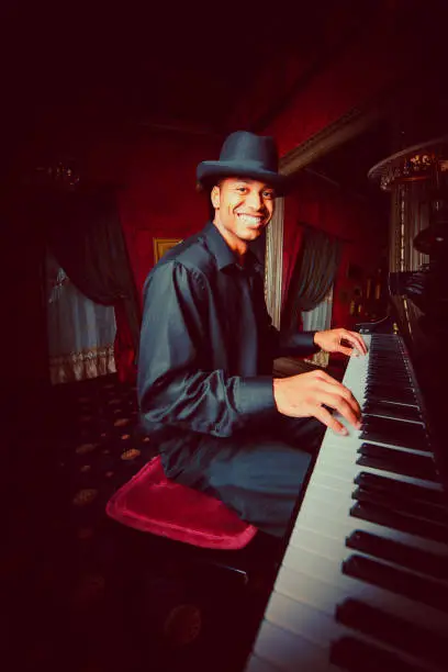Young african american musician playing grand piano in a posh nightclub, looking over with a bright smile. Ultra-Wide Angle Musician Nightclub Portrait.