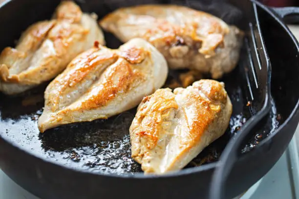 Photo of Fried chicken breasts on vegetable oil, iron cast pan