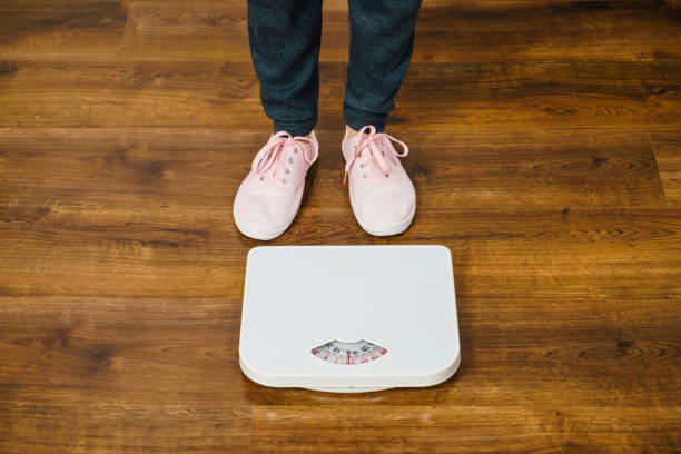 istock Woman with pink sneakers on bathroom weight scale 806897882