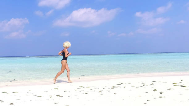 mujer en bikini corriendo por el agua en playa, maldivas - blond hair overcast sun sky fotografías e imágenes de stock