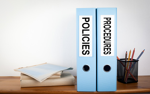 Policies and Procedures binders in the office. Stationery on a wooden shelf