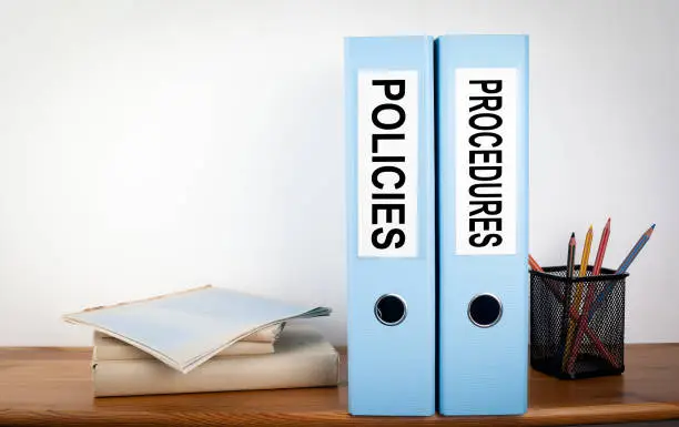 Photo of Policies and Procedures binders in the office. Stationery on a wooden shelf