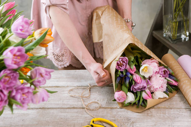 Female hand pack festive bouquet in wrapping paper