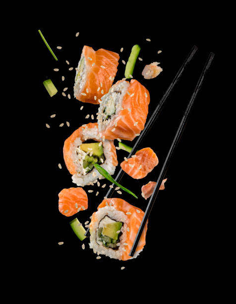 pezzi di sushi posizionati tra le bacchette su sfondo nero - sushi foto e immagini stock