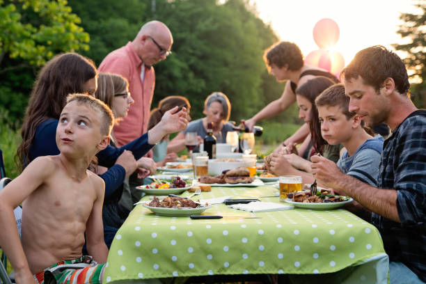 Big family barbecue gathering at sunset, summer outdoors. Celebration time for this three generation real family outdoors in summer. Big dinner is ready, people are eating at the table. Horizontal waist up shot with copy space. This was taken in Quebec, Canada. big family table stock pictures, royalty-free photos & images