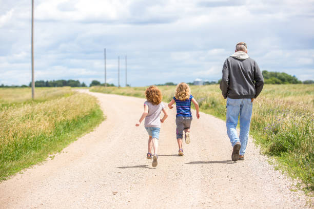 Girls & Grandpa Walking & Running Out Rural Gravel Driveway stock photo