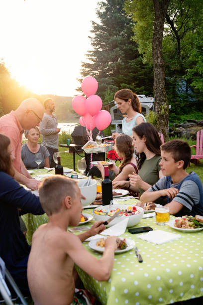 Big family barbecue gathering at sunset, summer outdoors. Celebration time for this three generation real family outdoors in summer. Big dinner is ready, people coming to the table. Horizontal waist up shot with copy space. This was taken in Quebec, Canada. big family sunset stock pictures, royalty-free photos & images