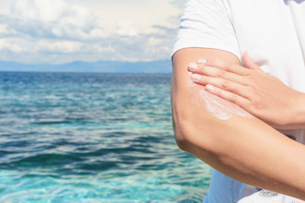 caucasian man applyng sun protector cream at her hand on the beach close to tropical turquoise sea under blue sky - spray tan body human skin imagens e fotografias de stock