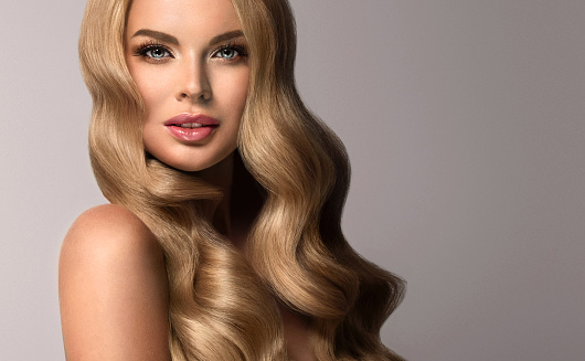 Young, blonde haired woman  with voluminous, shiny and wavy hair. Beautiful model with long, dense and curly hairstyle, vivid make-up and  pale rose lipstick on the lips.