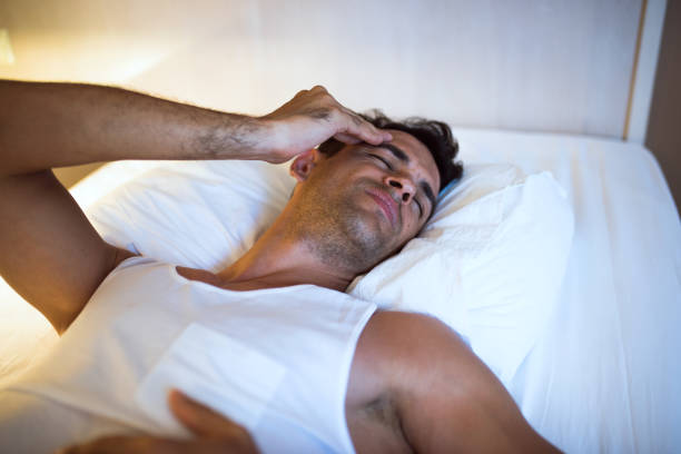 istock Handsome man having a headache lying on the white bed. Bedroom background. View from above 807022476