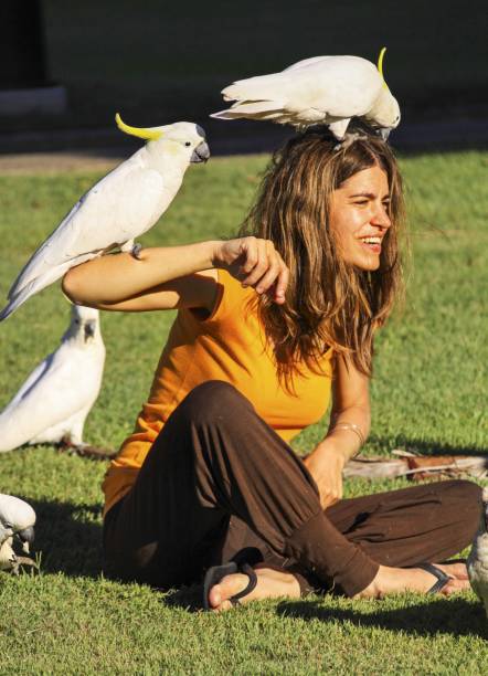 SYDNEY, AUSTRALIA - APRIL 2, 2010: Pretty Young Woman with Cockatoo Birds balancing on her shoulders sitting on the grass of Botanic Garden near Sydney Harbor