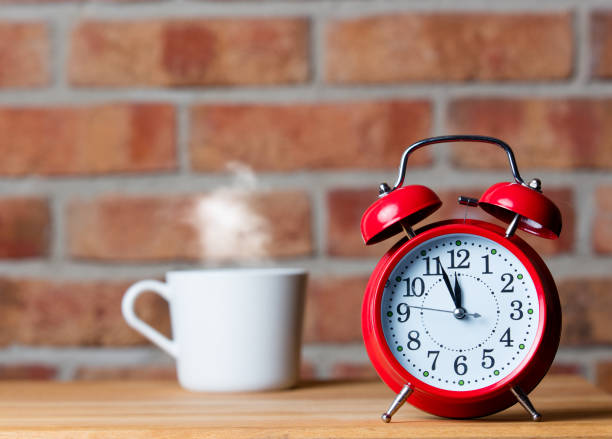 photo of cup of hot fresh coffee and red alarm clock on the wonderful brick wall background