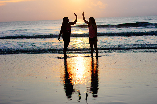 Two women high five each other at the beach.