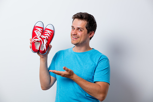Portrait of young man with red gumshoes in blue t-shirt on white background