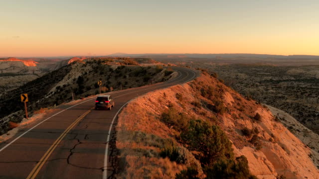 AERIAL: Black SUV car driving along the mountain ridge road at golden sunset