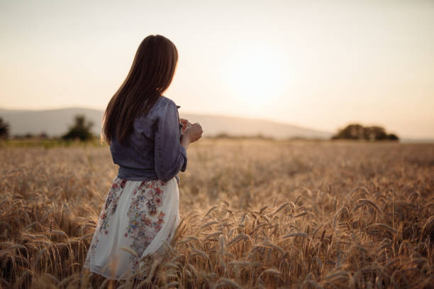 istock Young woman walking through wheat field during susnet 807147856