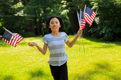 Smiling Asian girl running while holding American flags.