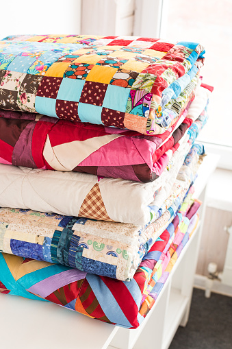 patchwork and fashion concept - beautiful stack of colorful quilts, bedspreads stacked in several rows in height for storage, sale of stitched products on a white background