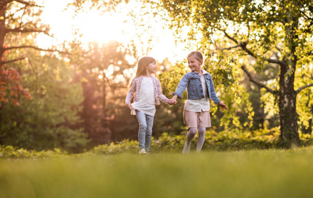 Full length of two carefree girls having fun while holding hands and running together during spring day.